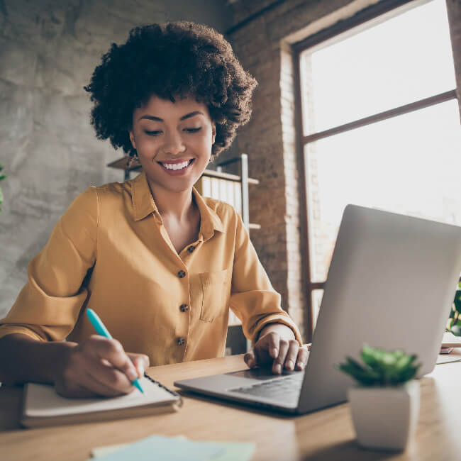 smiling woman writing notes while on her computer.