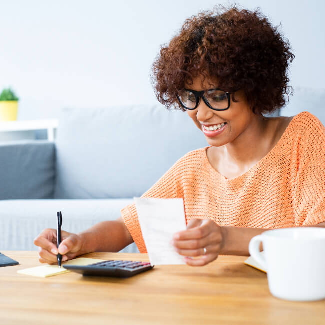 Smiling woman smiling with a calulator in front of her as she writes.